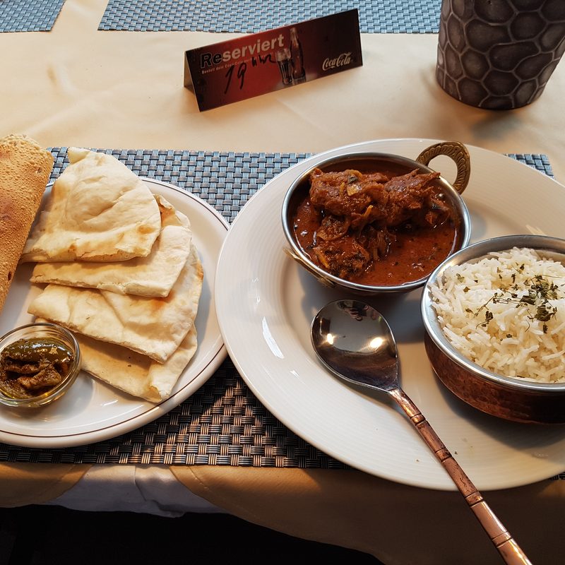 Curry in der Kupferschale mit Naan-Brot und Reis am Tisch